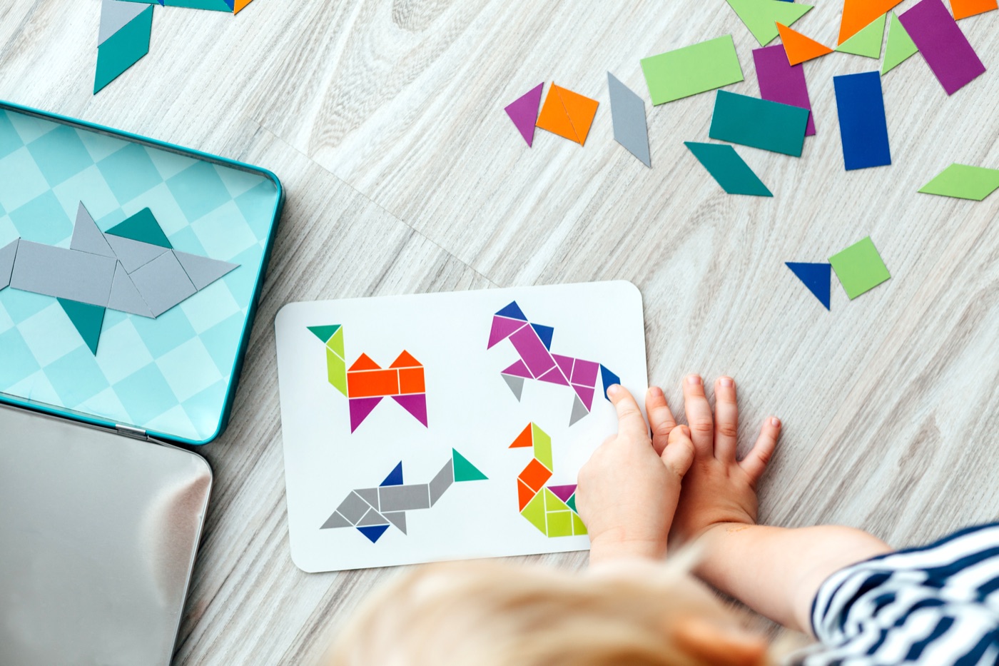 A child's hand arranging colorful tangram puzzle pieces